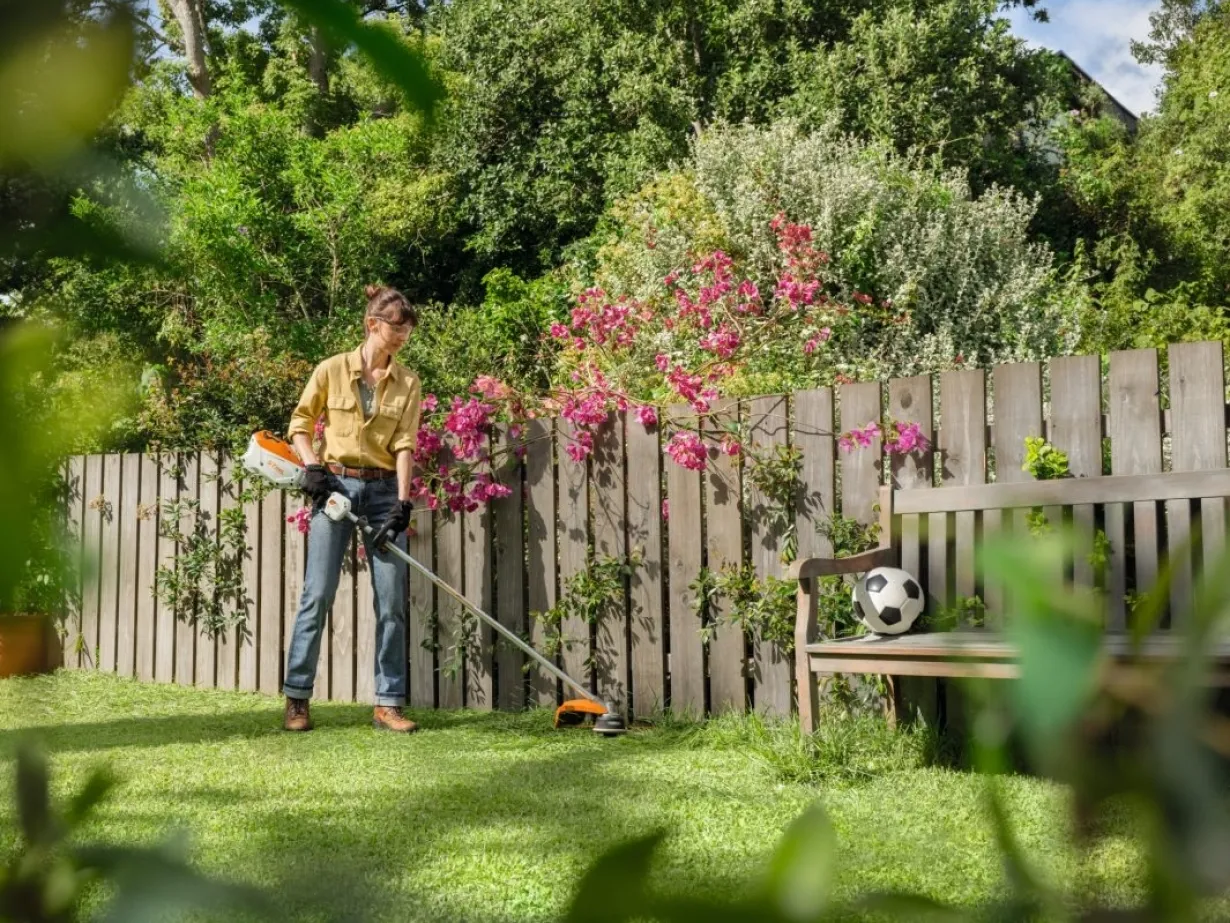 Femme passe la débroussailleuse dans un jardin