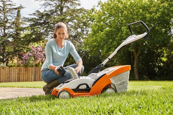 Une femme mettant une batterie dans la tondeuse STIHL